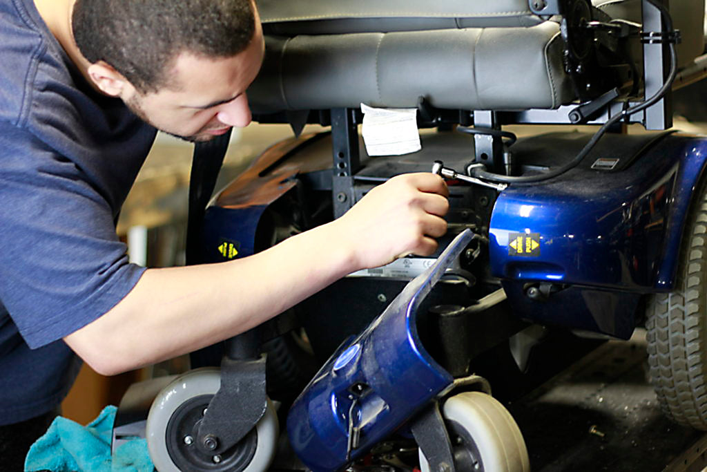 a technician leans in to make adjustments to the base of a blue power wheelchair