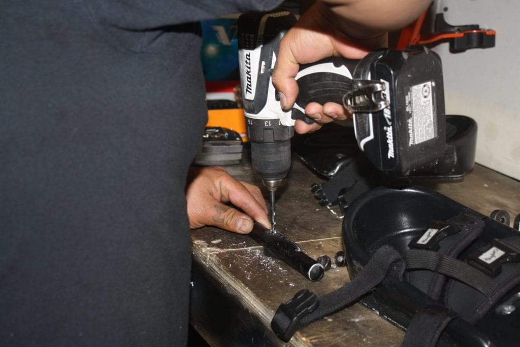 a close-up view of a mobility specialist using a power drill to put holes in a piece of metal tubing as part of a wheelchair customization