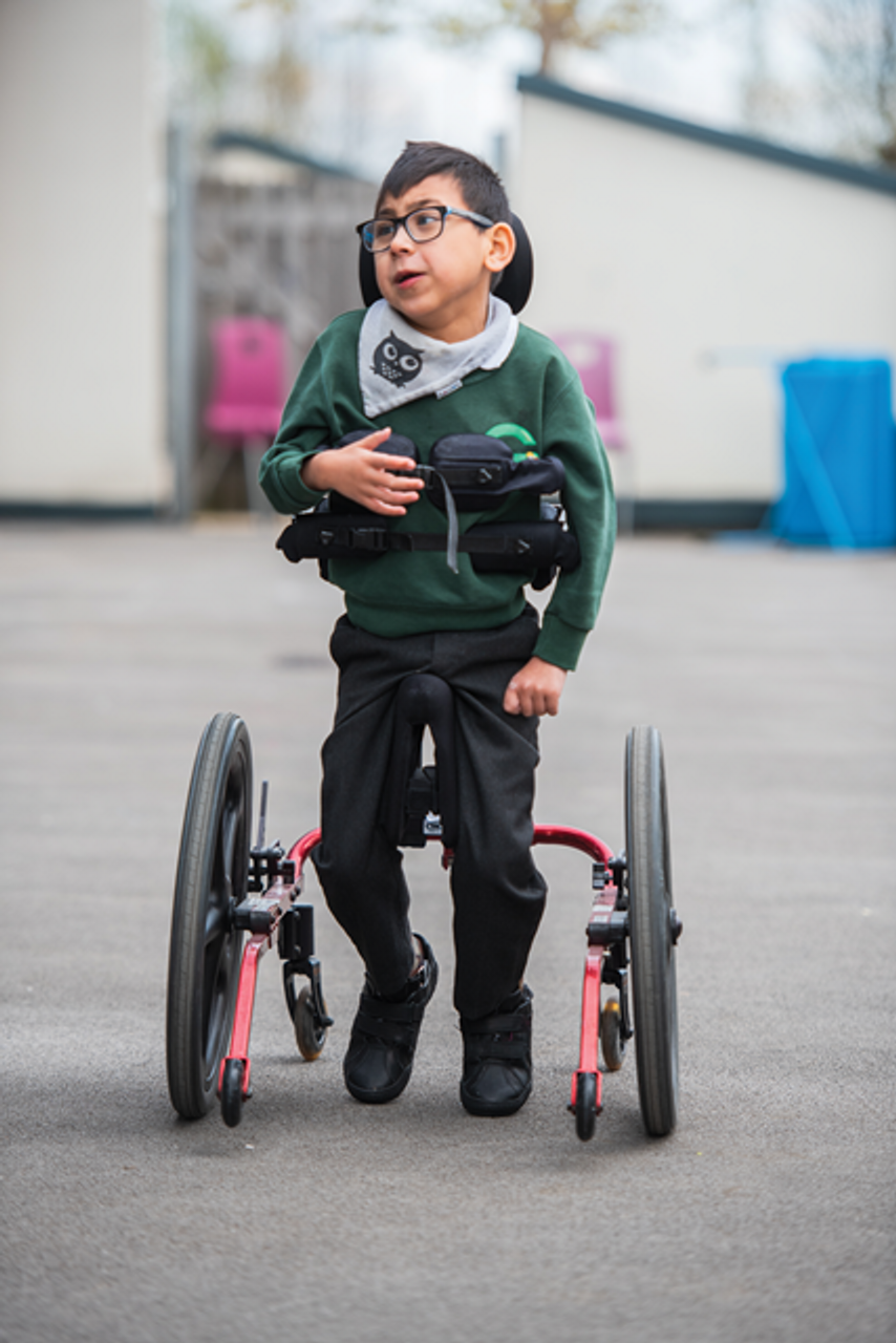 Child in a green sweater and black pants using a KidWalk on a concrete surface.