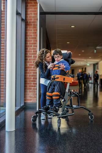 Woman interacting with a child in a Leckey Mygo in a hallway.
