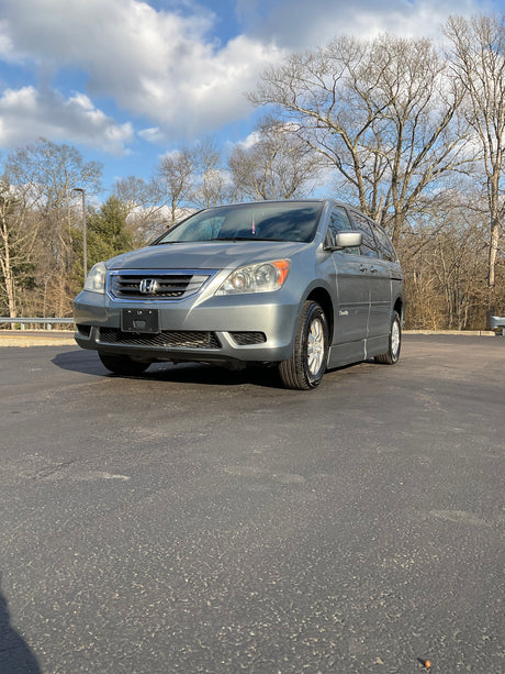 Silver Honda Odyssey parked on a paved road with trees and blue sky in the background