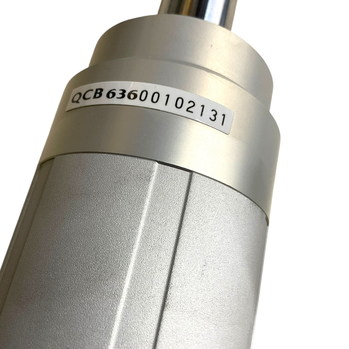 Close-up of a metallic cylindrical industrial component with a white label printed with the code QCB63600102131, on a plain white background.