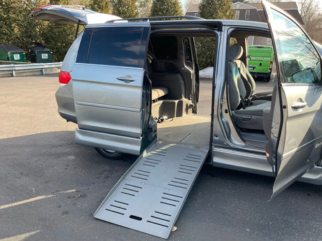 Honda Odyssey with open doors and a wheelchair ramp extended in a parking lot.