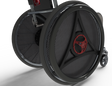 Close-up of large black carbon-fiber-look wheelchair wheels with red circular center accents and a small caster wheel, shown on a white studio background.