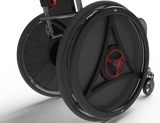 Close-up of large black carbon-fiber-look wheelchair wheels with red circular center accents and a small caster wheel, shown on a white studio background.